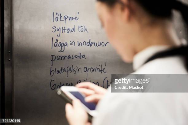 rear view of female chef using mobile phone with text on metal in commercial kitchen - langues étrangères photos et images de collection