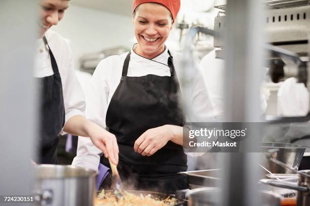 teacher watching female chef student cooking food in kitchen at restaurant - kochlehrling stock-fotos und bilder