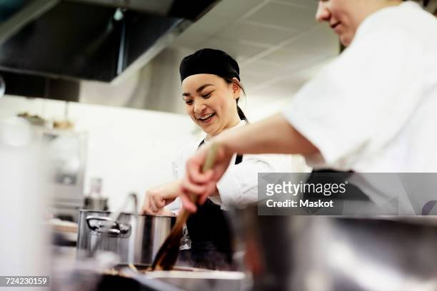 smiling female chef student with colleague cooking food in commercial kitchen - cocina comercial fotografías e imágenes de stock