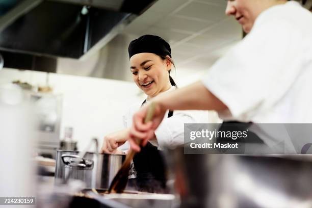 smiling female chef student with colleague cooking food in commercial kitchen - restaurant kitchen ストックフォトと画像