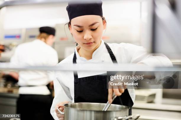 young female chef stirring pot in kitchen at restaurant - kochlehrling stock-fotos und bilder