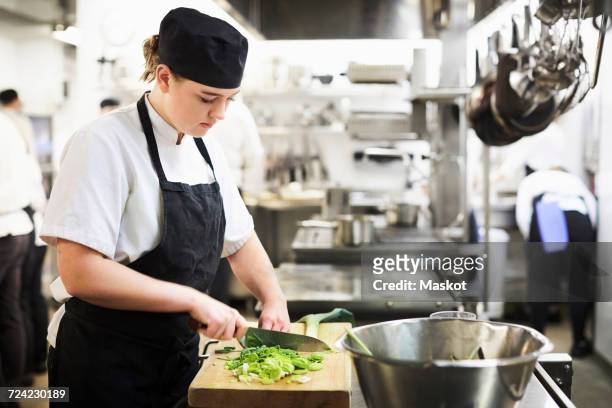 young female chef chopping vegetables on cutting board in cooking school - restaurant kitchen stock-fotos und bilder