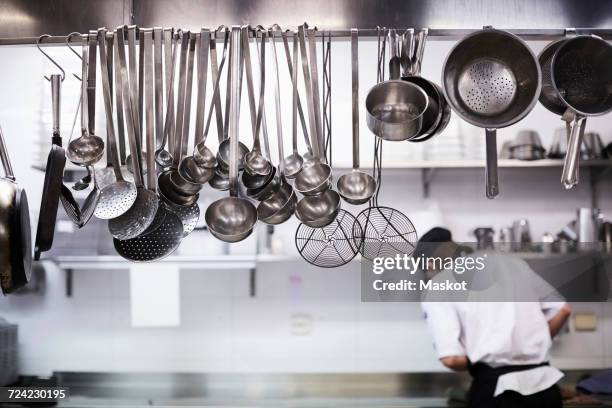 utensils on metal rack with chef cooking in background at commercial kitchen - stage set stockfoto's en -beelden