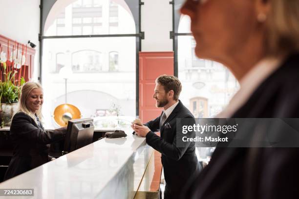 happy businessman talking to female receptionist at hotel reception - corporate business transaction stock pictures, royalty-free photos & images