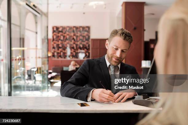 mature businessman paying through credit card at hotel reception - accueil hotel photos et images de collection