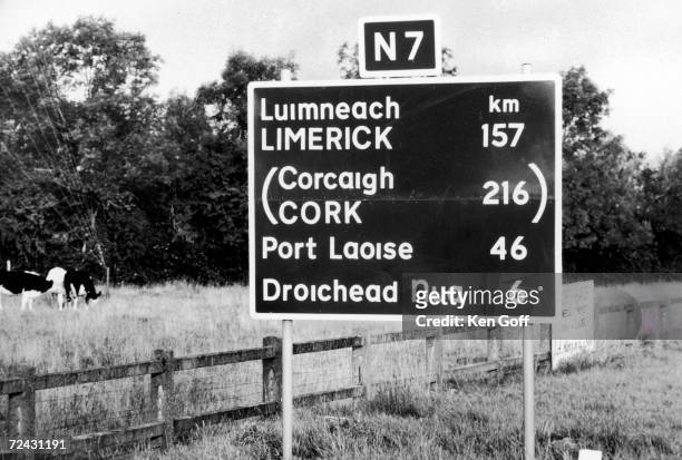 Traffic sign with the distances in kilometers and the names LIMERIC, CORK and PORT LAOISE in both English and Gaelic.