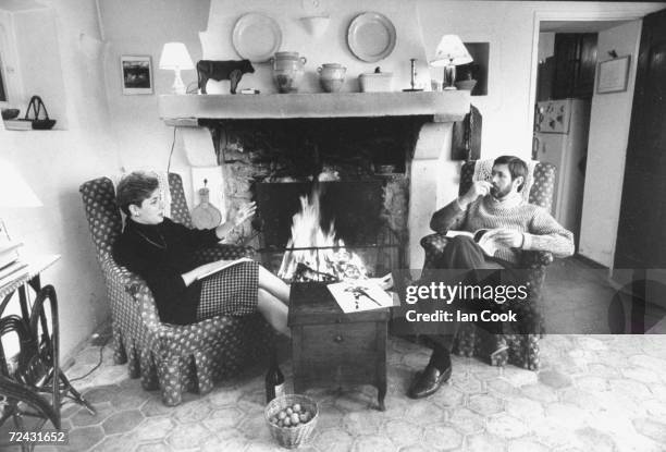 International Herald Tribune editor Walter Wells with wife Patricia, food critic, at French provincial home reading by fireplace.