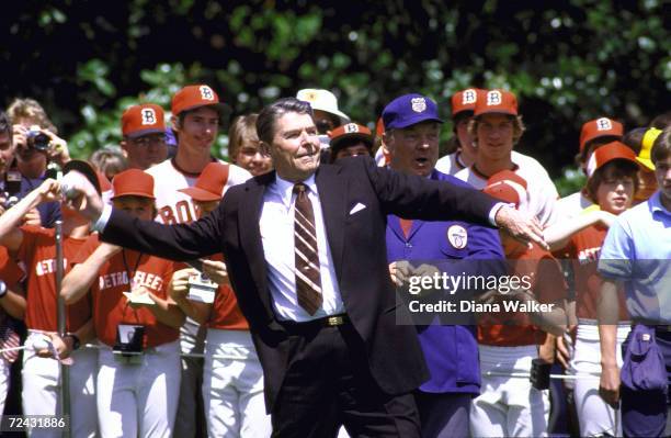 President Ronald Reagan winding up for opening pitch of Little League football game with players behind him.