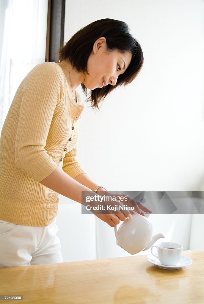 A mid adult woman pouring tea into a cup