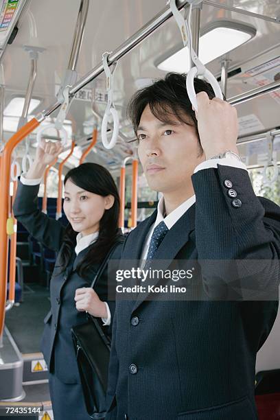 a young woman and a mid adult man standing in a bus - つり革 ストックフォトと画像