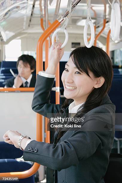 a young woman checking watch in a bus - つり革 ストックフォトと画像
