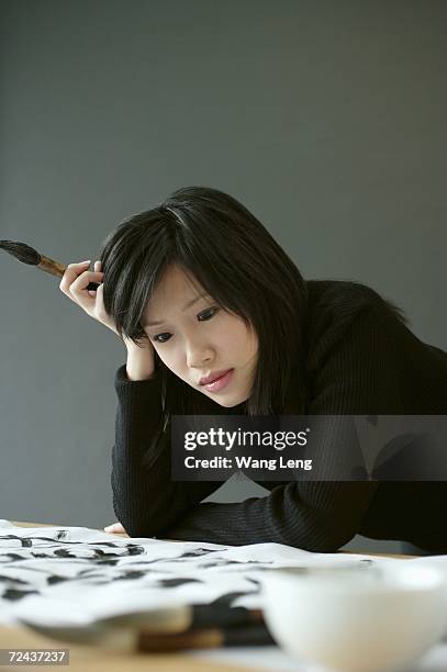 woman holding paintbrush, leaning head on hand - head on table stock-fotos und bilder