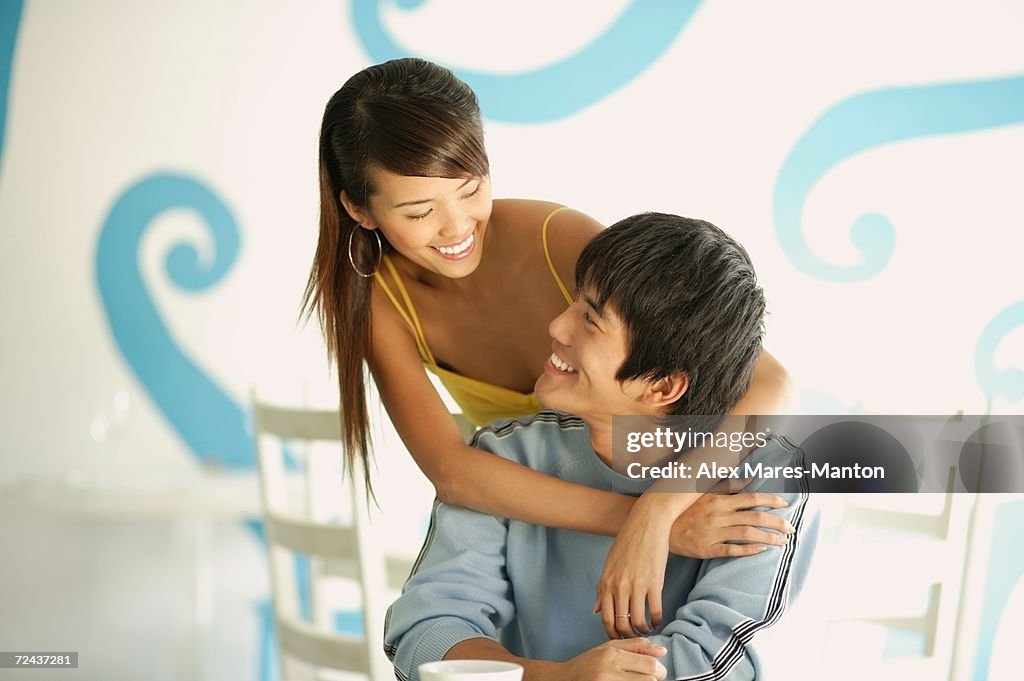 Woman standing behind seated man, embracing him from behind