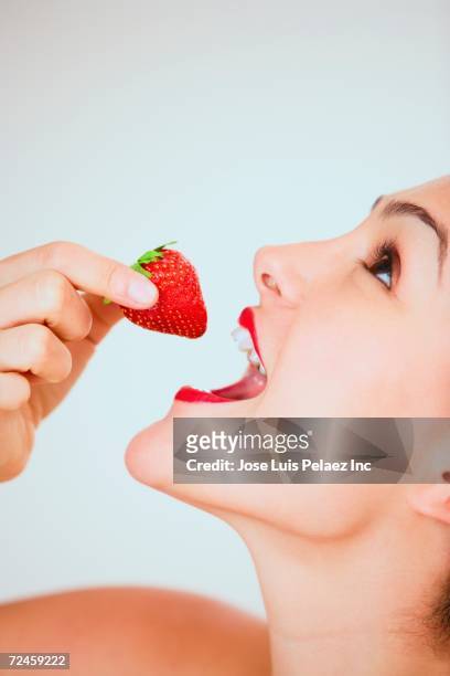 close up studio shot of hispanic woman about to eat strawberry - femme visage beauté profil fond blanc photos et images de collection