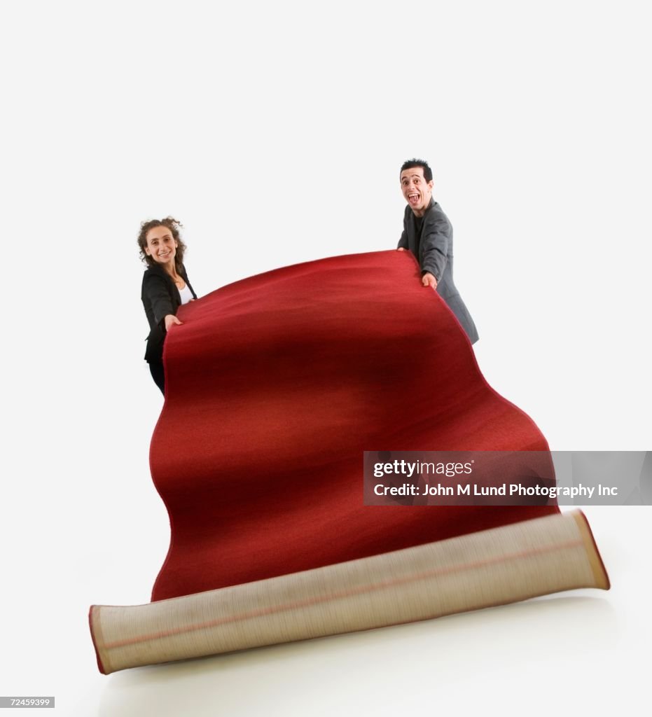 Studio shot of man and woman unrolling red carpet