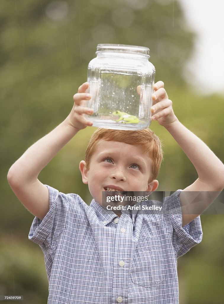 Young boy looking at frog in glass jar outdoors