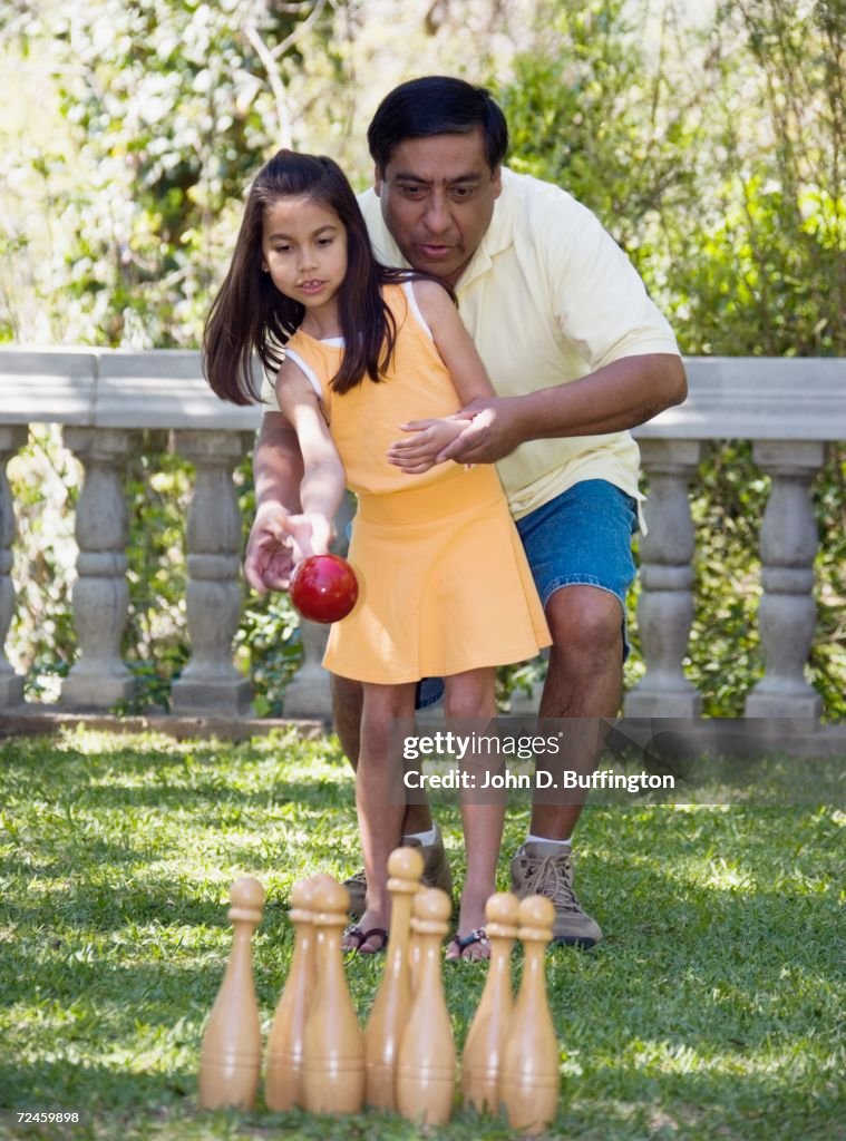 Hispanic father helping daughter play lawn bowling