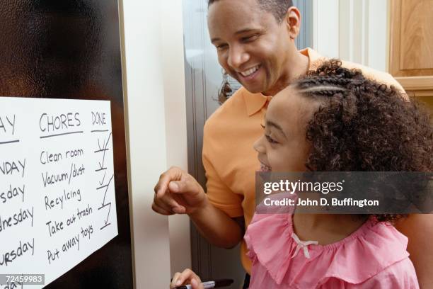 african father and daughter looking at chores chart - chores stock-fotos und bilder