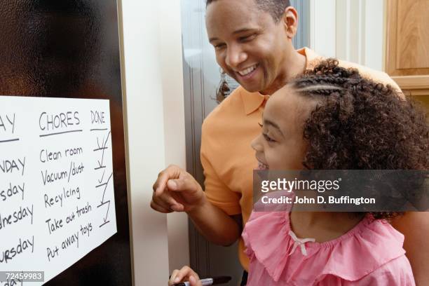 african father and daughter looking at chores chart - domestic chores photos et images de collection