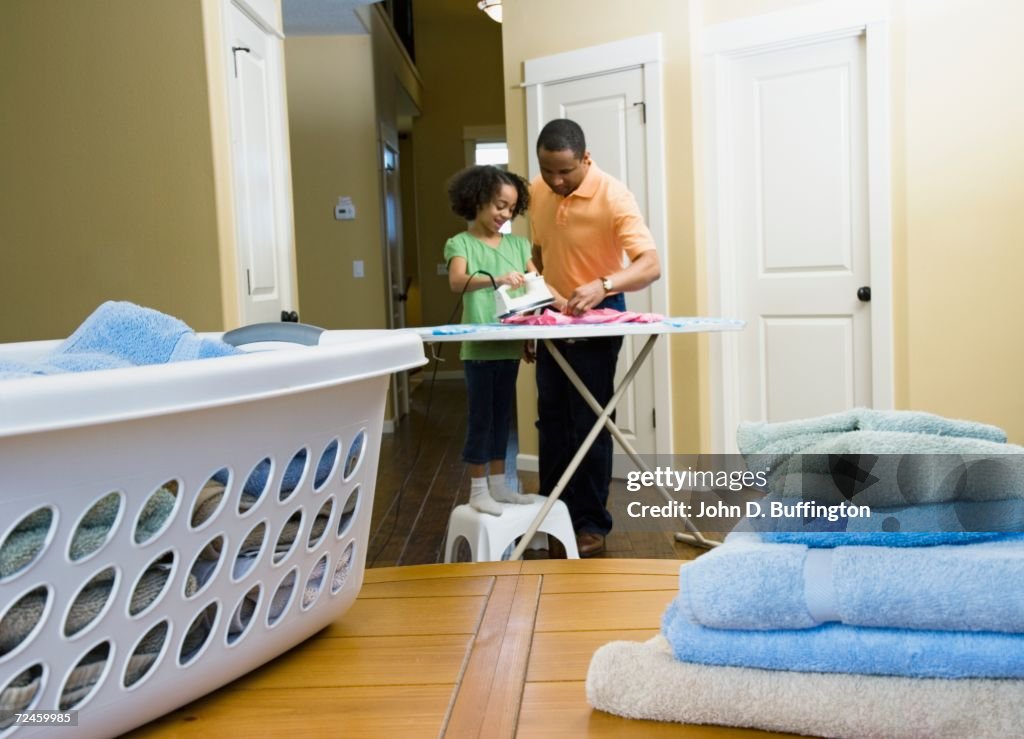 African father and daughter using iron in laundry room