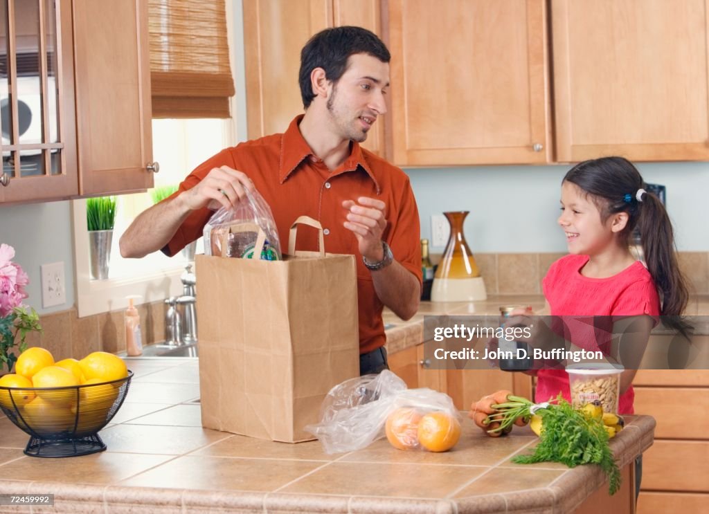 Hispanic father and daughter unpacking groceries in kitchen