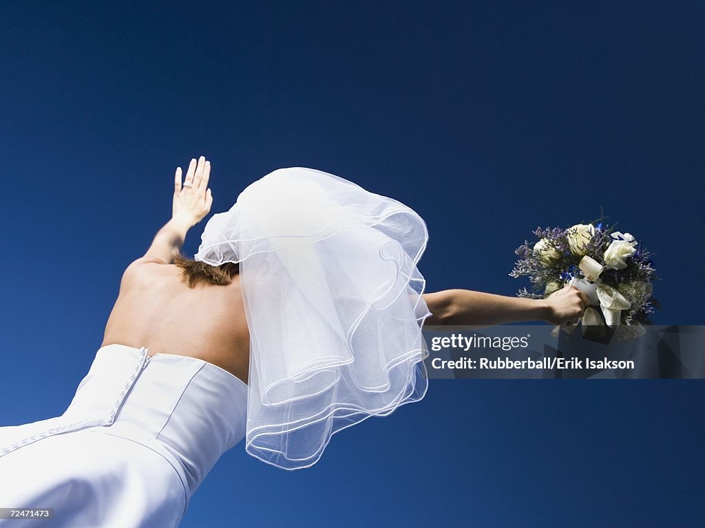 Low angle view of a bride holding a bouquet of flowers with her arms raised