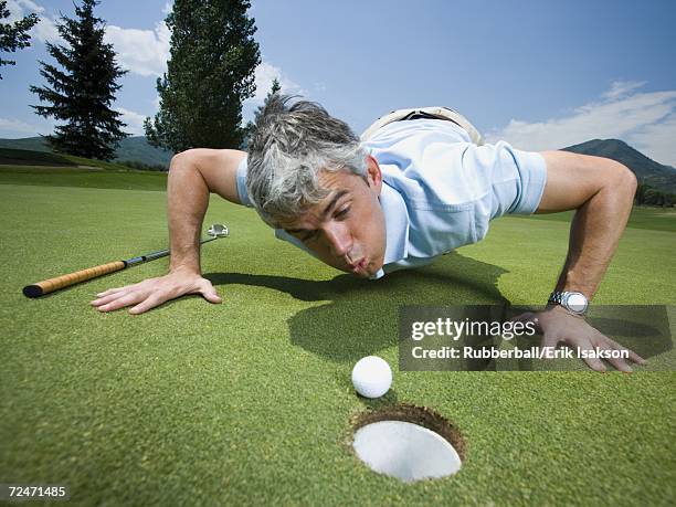 close-up of a man blowing a golf ball towards a hole - golf cheating stock pictures, royalty-free photos & images