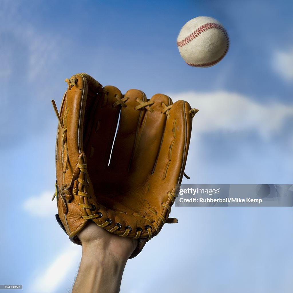 Low angle view of a person's hand catching a baseball with a baseball glove