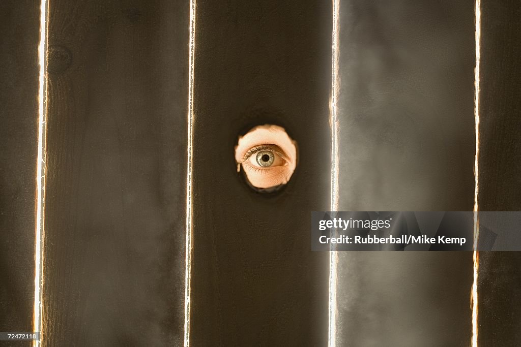 Woman peeping through hole in fence