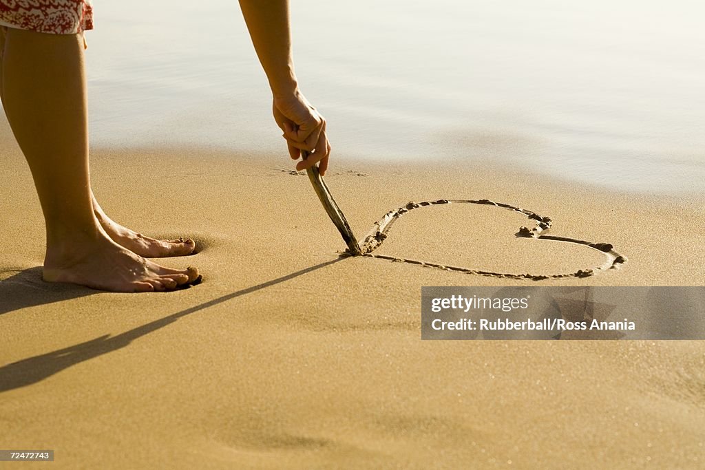 Low section view of a person drawing a heart in the sand on the beach