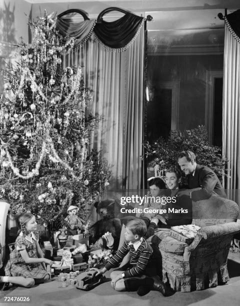 1950s: Family gathered around Christmas tree with gifts.