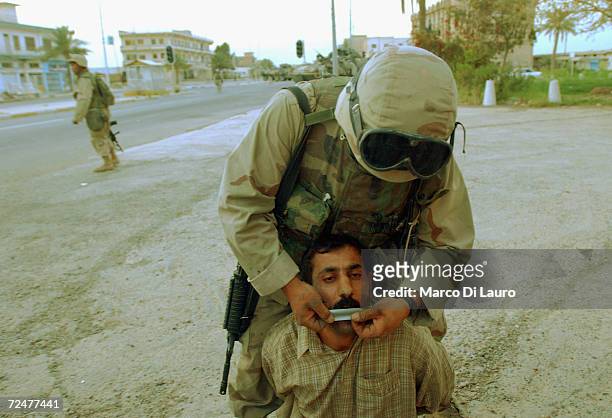 Marine puts tape over the mouth of an Iraqi prisoner of war in the main Square of Tikrit, April 14, 2003 some175 kilometers - just over 100 miles -...