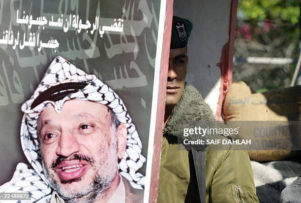 Palestinian security officer stands in the shade close to a poster of the late Palestinian leader Yasser Arafat at the Muqataa or Palestinian...