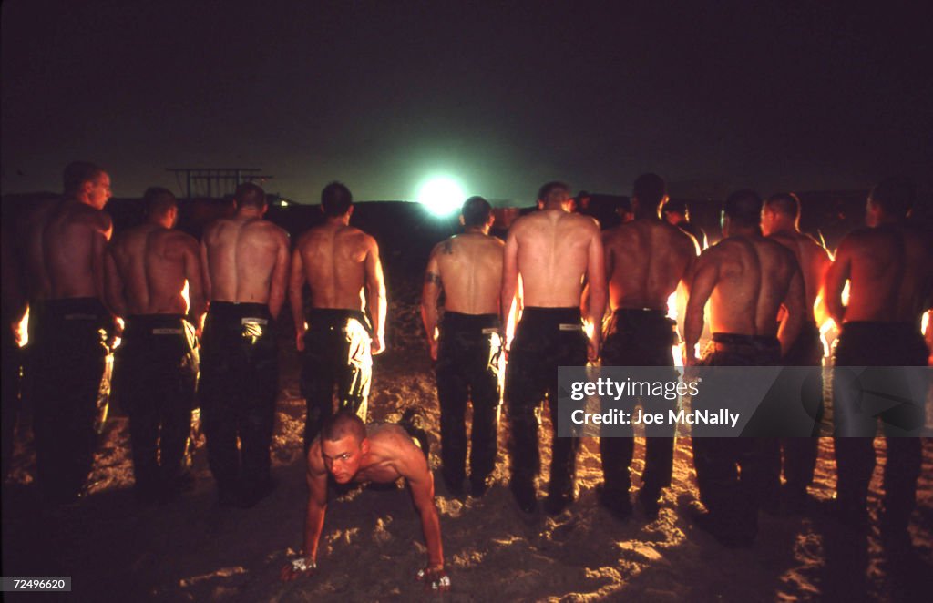 Hell Week Training Program A Navy Seal trainee executes pushups in the sand as other trainees ...