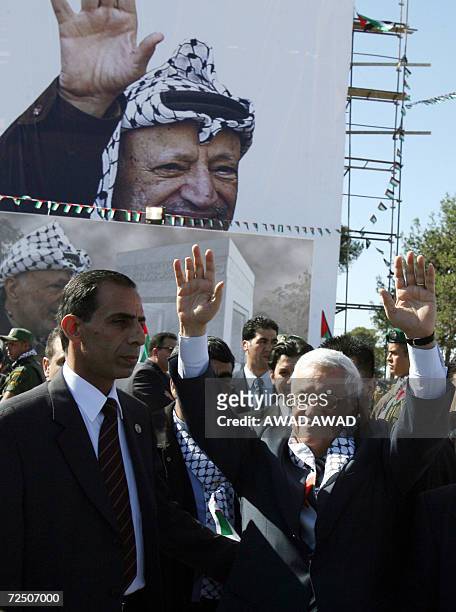 Palestinian President Mahmud Abbas raises his hands to the crowd in front of a giant portrait of Palestinian patriarch Yasser Arafat wearing his...