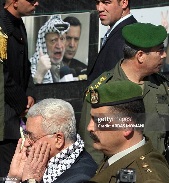 Palestinian President Mahmud Abbas , flanked by security guards, stands under a portrait of Yasser Afafat during a ceremony commemorating the second...