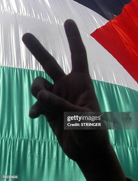 Palestinian man, supporter of the Fatah party, shows the V-sign for victory as he stands in front of the national flag during a rally marking the...