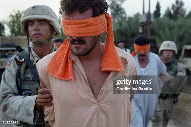 Army soldiers from the 299th Engineering Battalion, 4th Infantry Division blindfold detained Iraqi man and load them into a truck after suspecting...