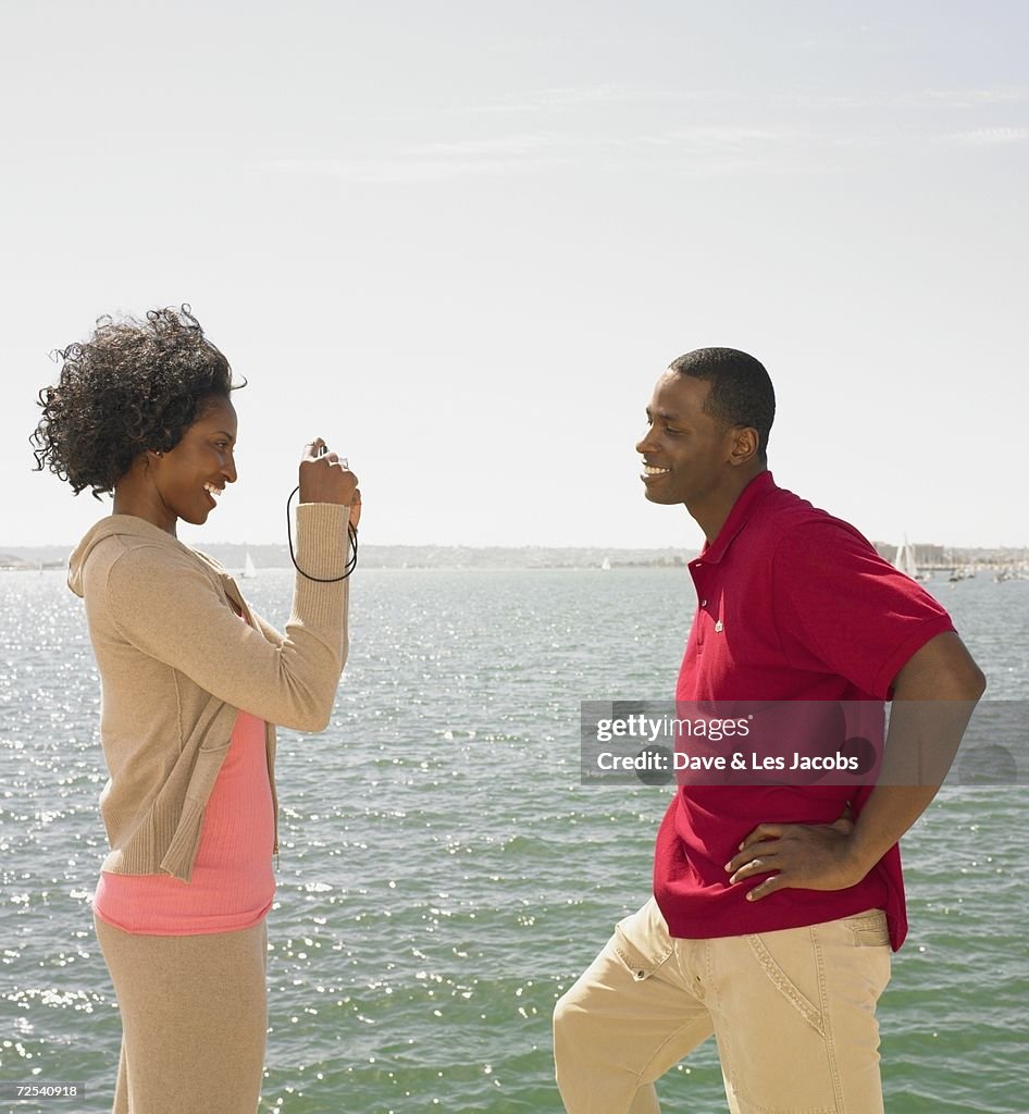 African woman taking photograph of African man next to water