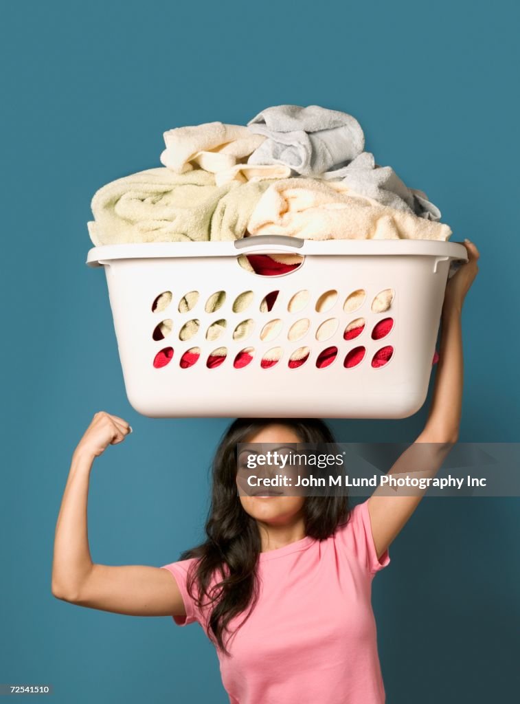 Hispanic woman flexing biceps and holding laundry basket on head