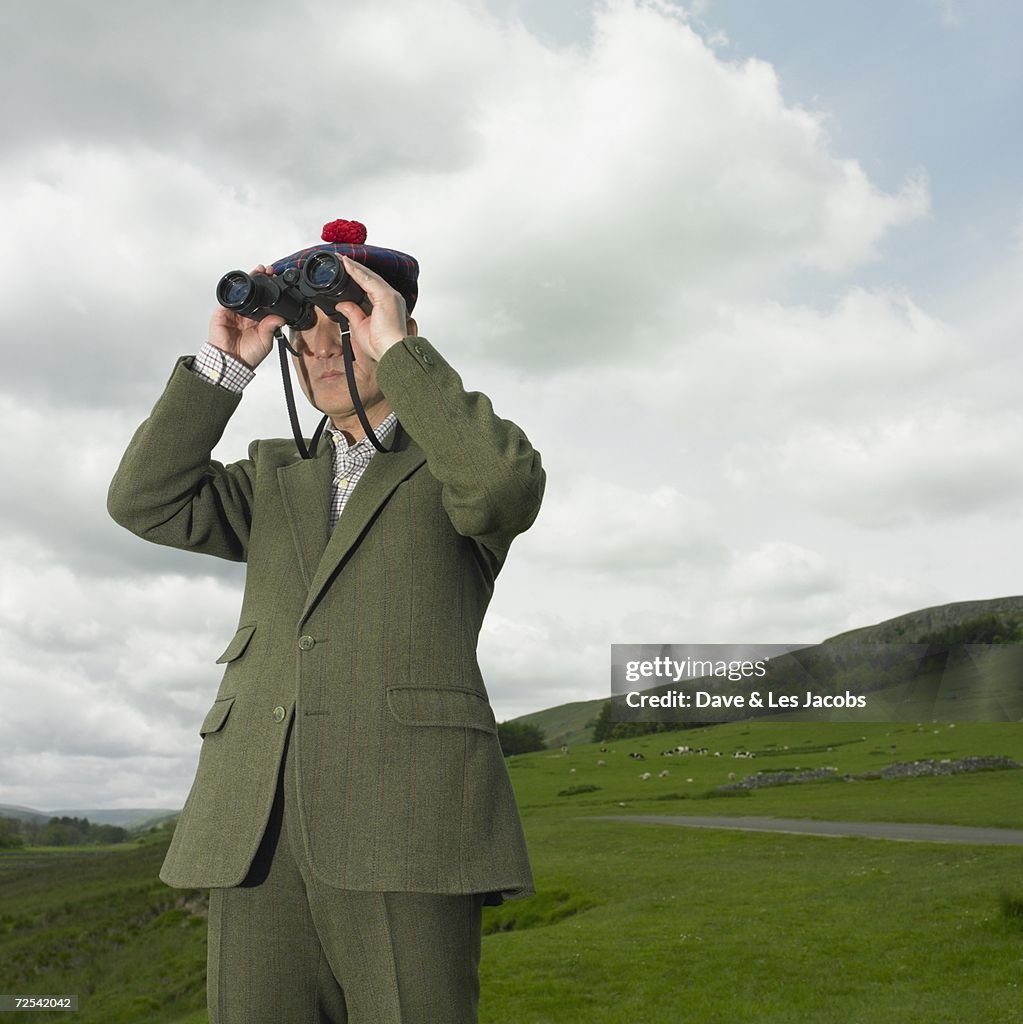 Man in tweed suit looking through binoculars in countryside
