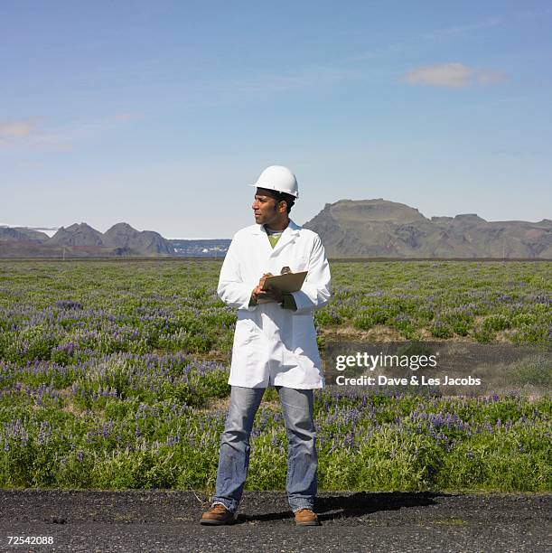 man with hard hat and clipboard standing on side of deserted road - scientist full length stock pictures, royalty-free photos & images