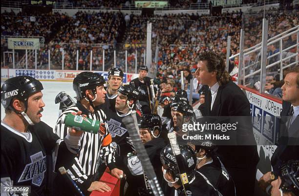Canadian ice hockey coach Barry Melrose of the Los Angeles Kings shares words with an official during a game while his team listens in, February 1995.