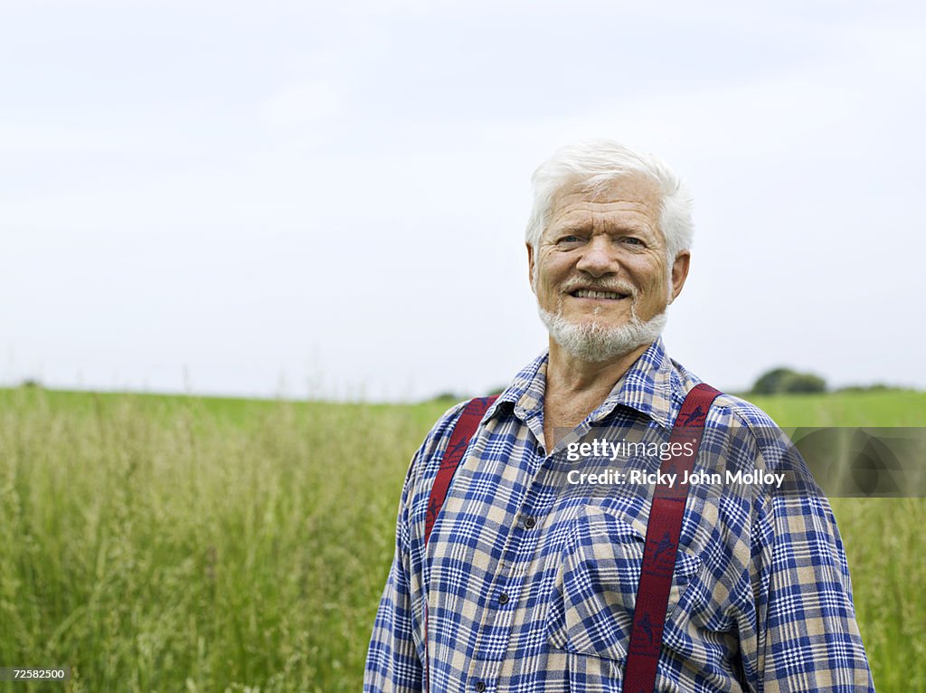 Senior man in long grass, smiling, portrait