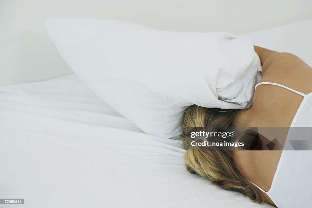 Woman lying on bed, head under pillow