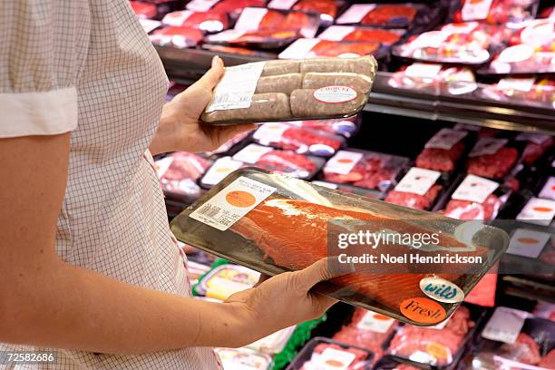 woman holding sausages and fish in supermarket, mid section - meat packaging stockfoto's en -beelden