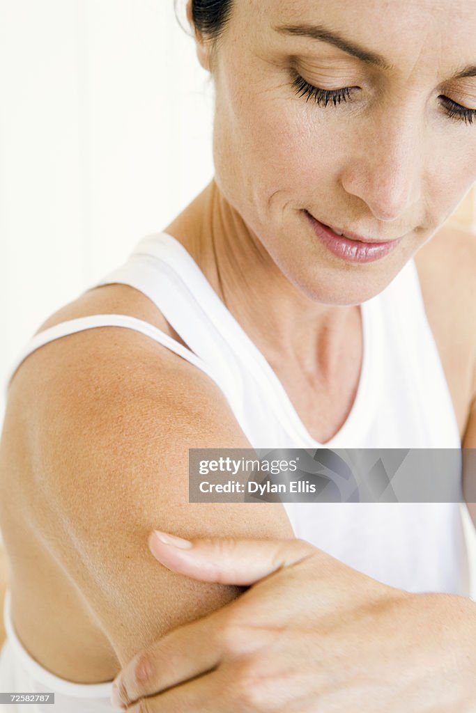 Woman applying moisturiser on arm, close-up, smiling