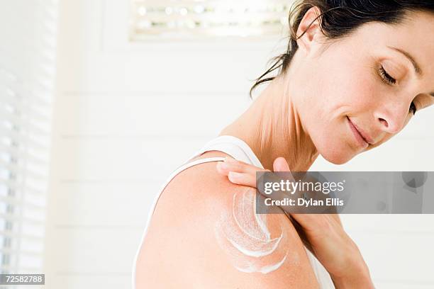 woman applying moisturiser on arm, smiling - bodylotion stock pictures, royalty-free photos & images