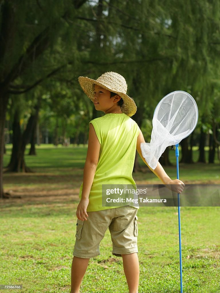 Rear view of a boy holding a butterfly net and looking sideways
