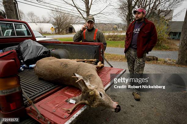 Vermont state wildlife biologist, not shown, records the data from a recently shot whitetail deer as the hunter, Ron Daniels, center, and his hunting...